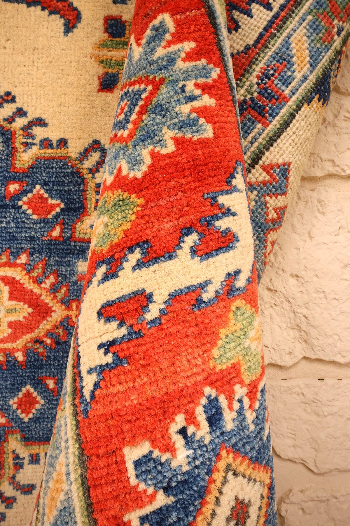Coin replié du tapis Kazak en laine nouée main, motifs bleus sur fond rouge