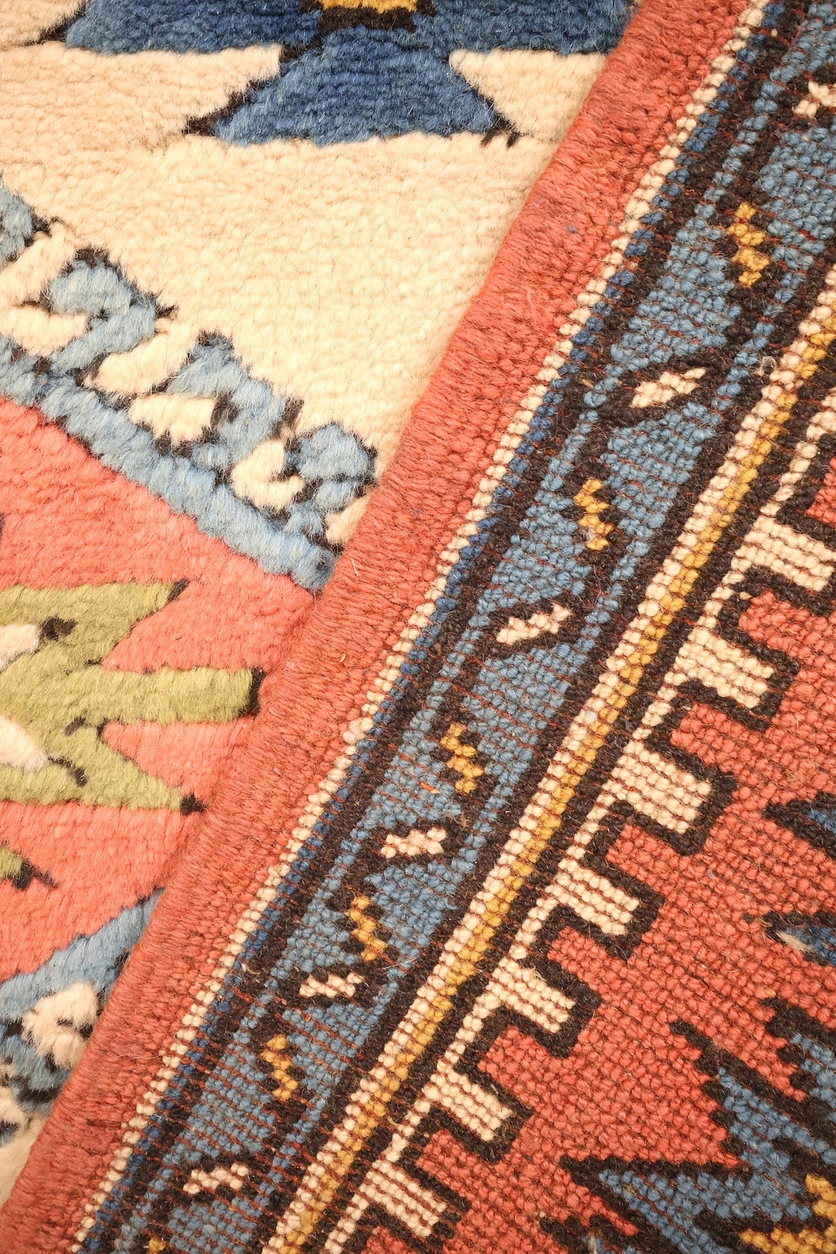 Coin replié du tapis Konya, passage du champ beige aux bordures rouge et bleue