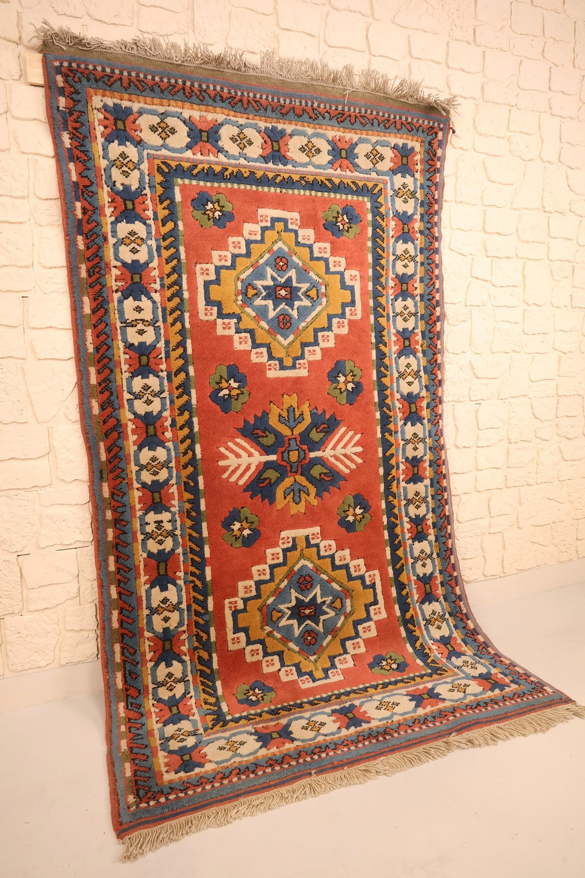 Tapis Konya rectangulaire 205 × 116 cm vu de biais, champ rouge corail et bordure ivoire