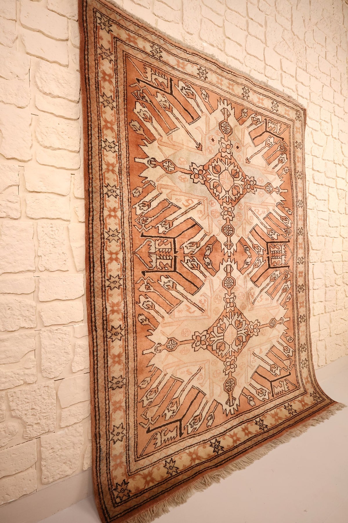 Tapis Kula rectangulaire orange et beige, vue de biais contre un mur clair