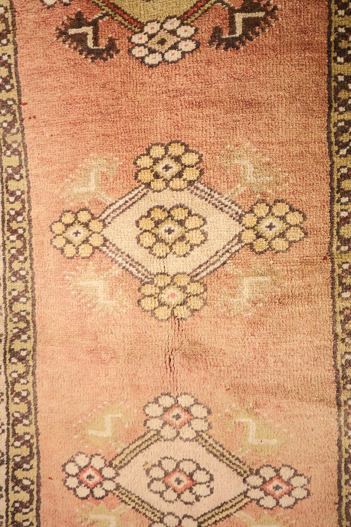 Détail des médaillons clairs à rosettes jaunes sur le champ rose du tapis Melas
