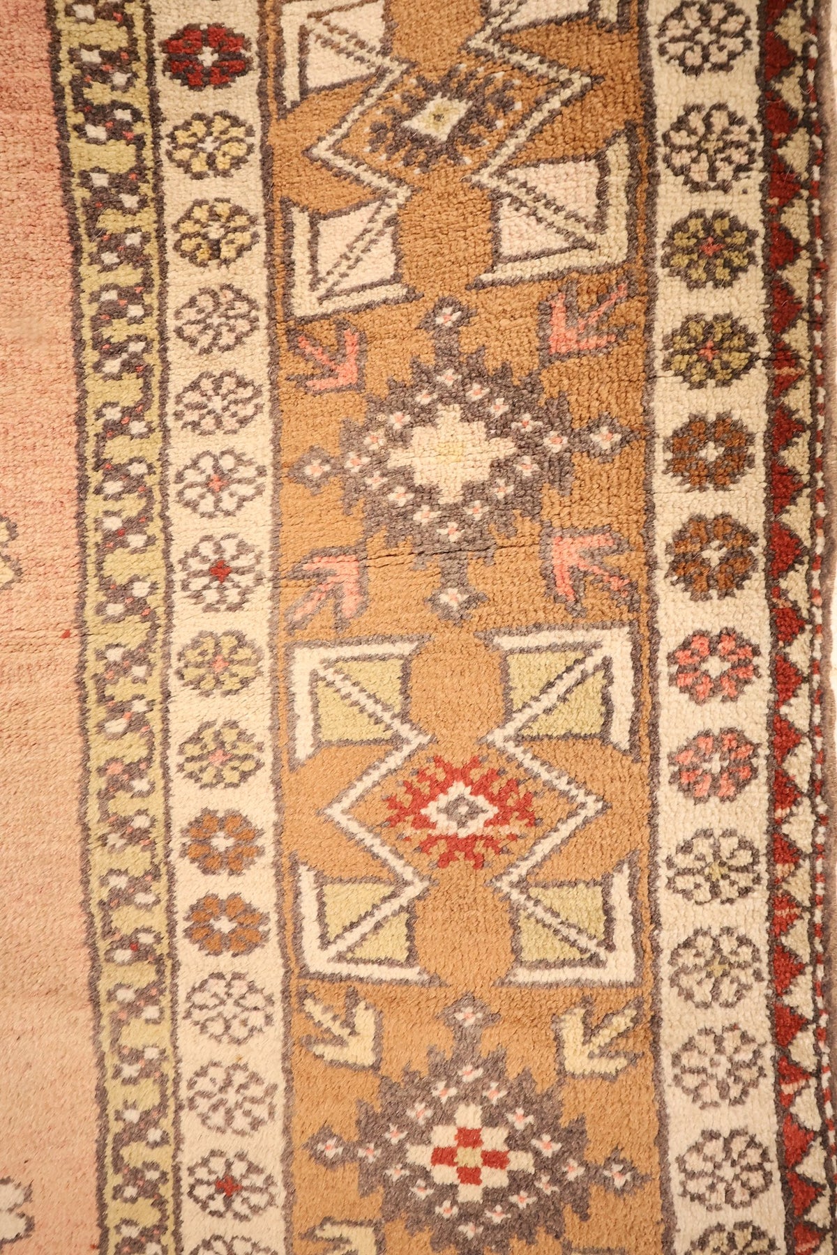 Bordure brun clair du tapis Melas, losanges crénelés, étoiles et rosettes ivoire