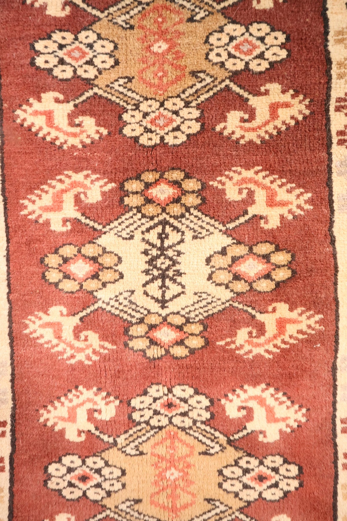 Détail des médaillons losangés beige et ocre sur fond rouge du tapis Melas