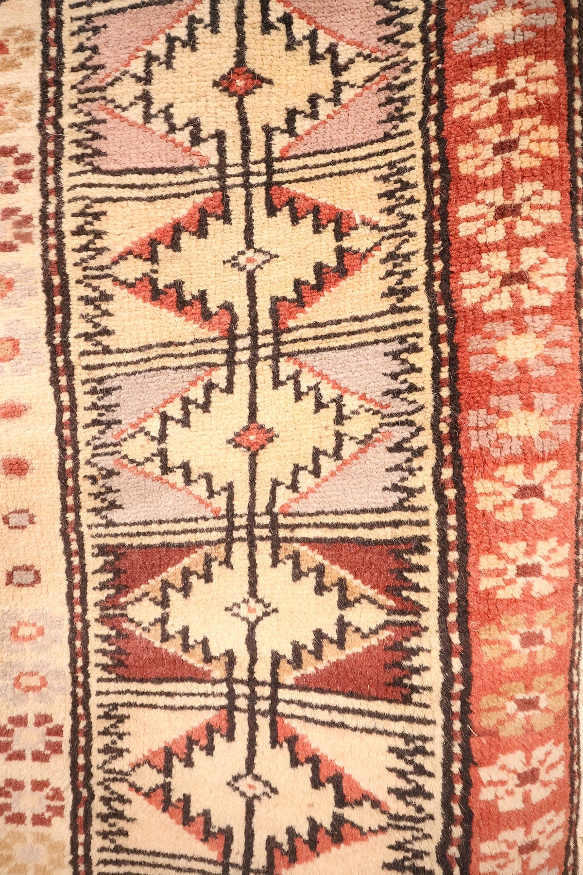 Bordure beige à losanges dentelés rouges et gris-violet, galon rouge fleuri du tapis Melas