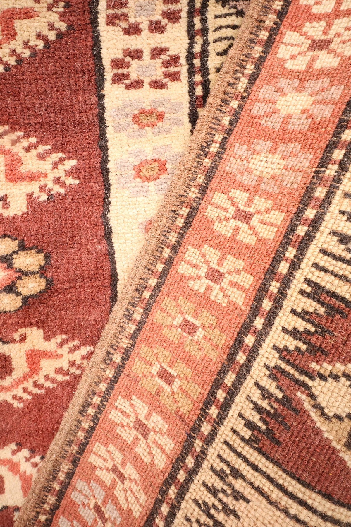 Coin replié du tapis Melas, galons étroits crème et rouge le long de la lisière