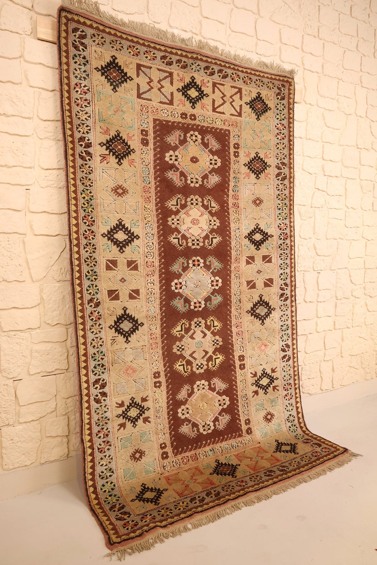 Tapis Melas en laine noué à la main, vue de biais contre un mur clair