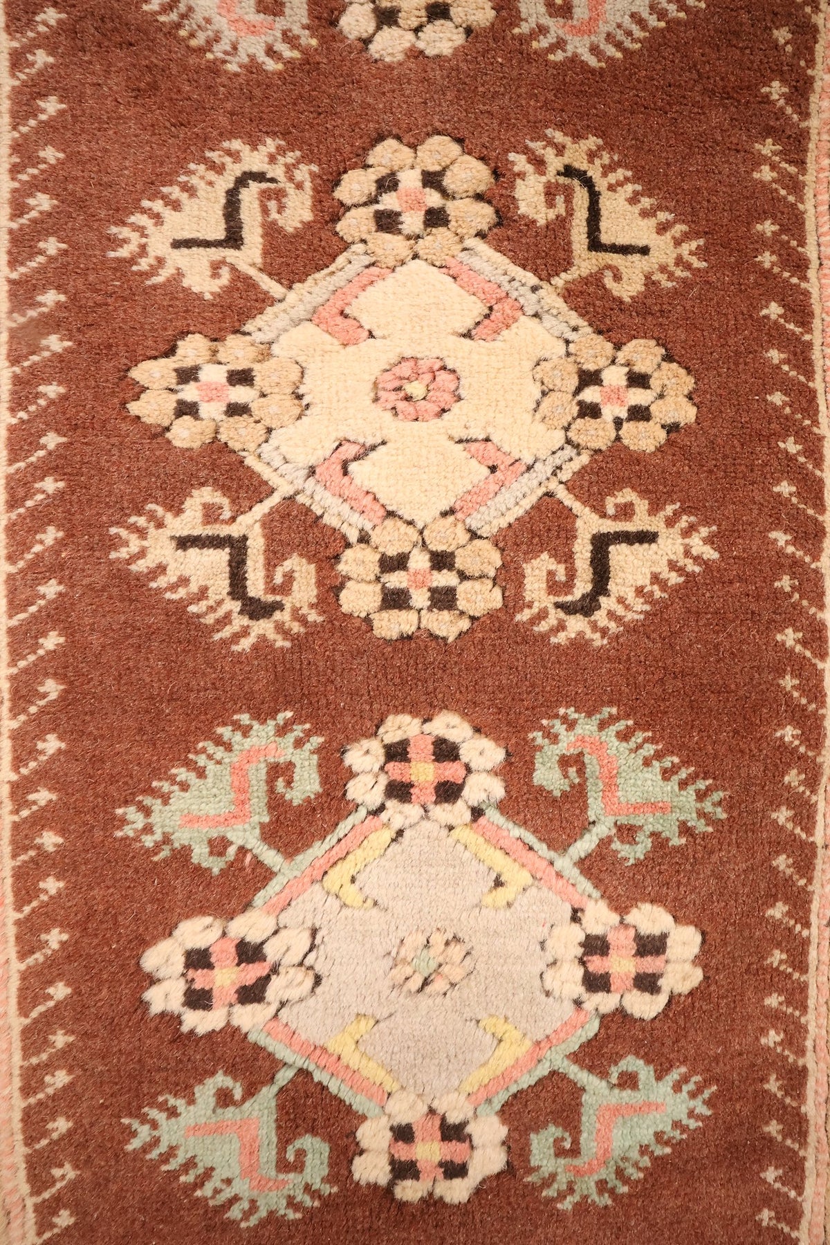 Détail des médaillons losangés beige, gris et rose sur le champ brun du Melas