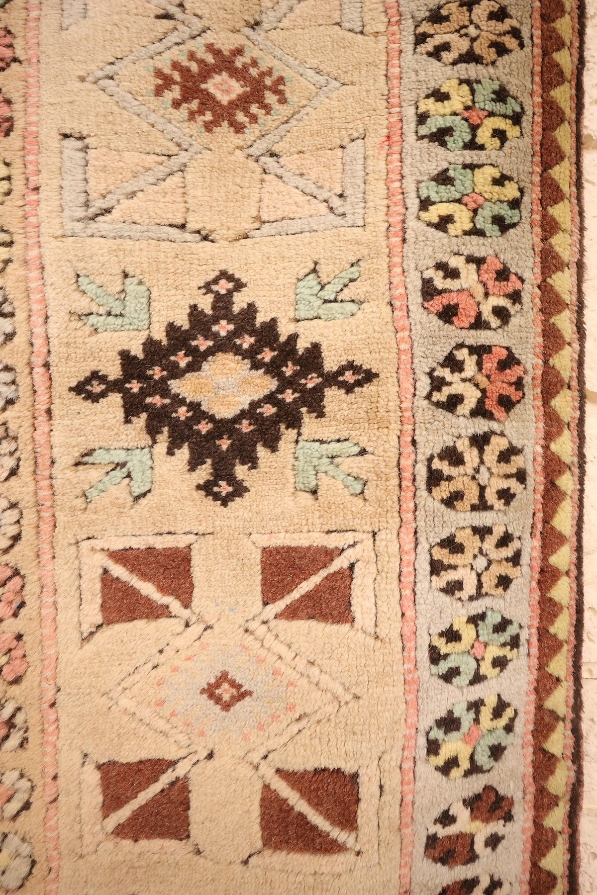 Bordure du tapis Melas : bande beige à étoiles crantées et rosettes rondes multicolores