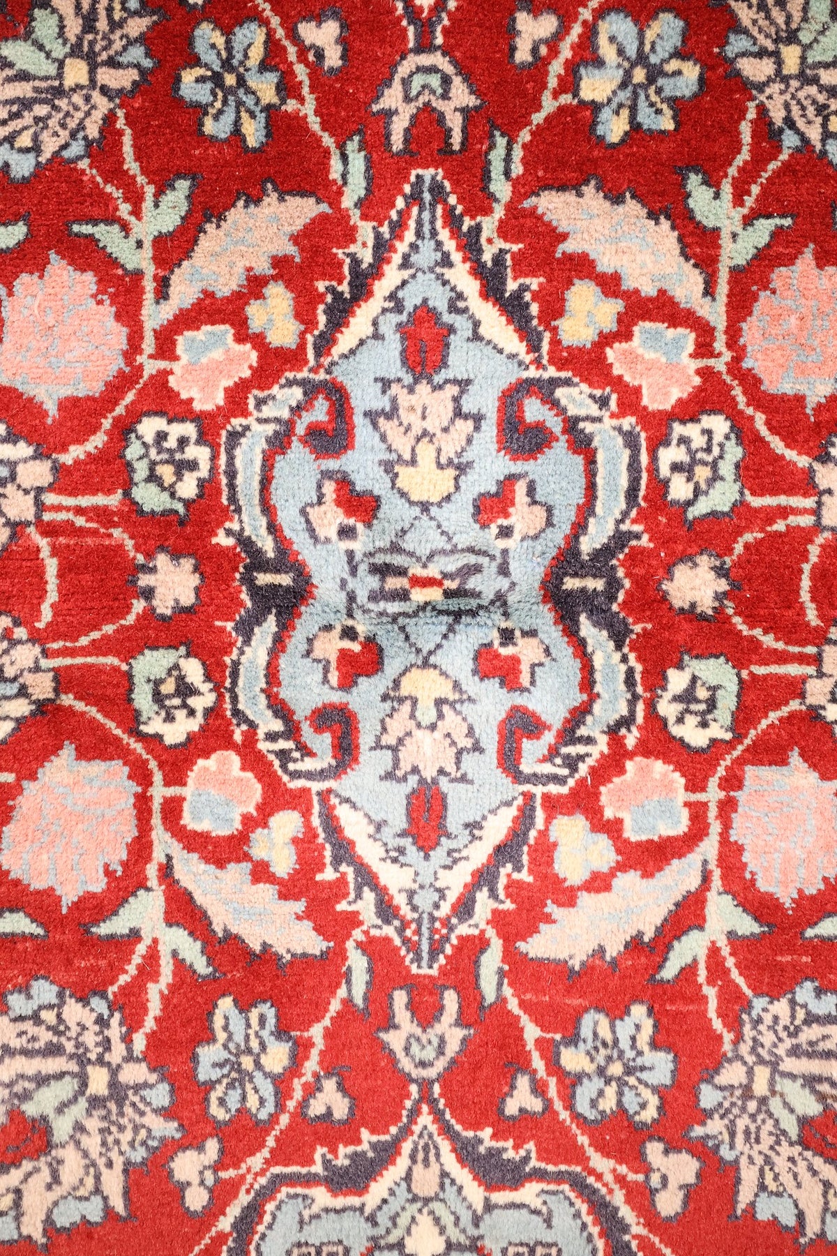 Détail du médaillon bleu clair à pendentifs et des tiges fleuries du tapis Pendjab rouge