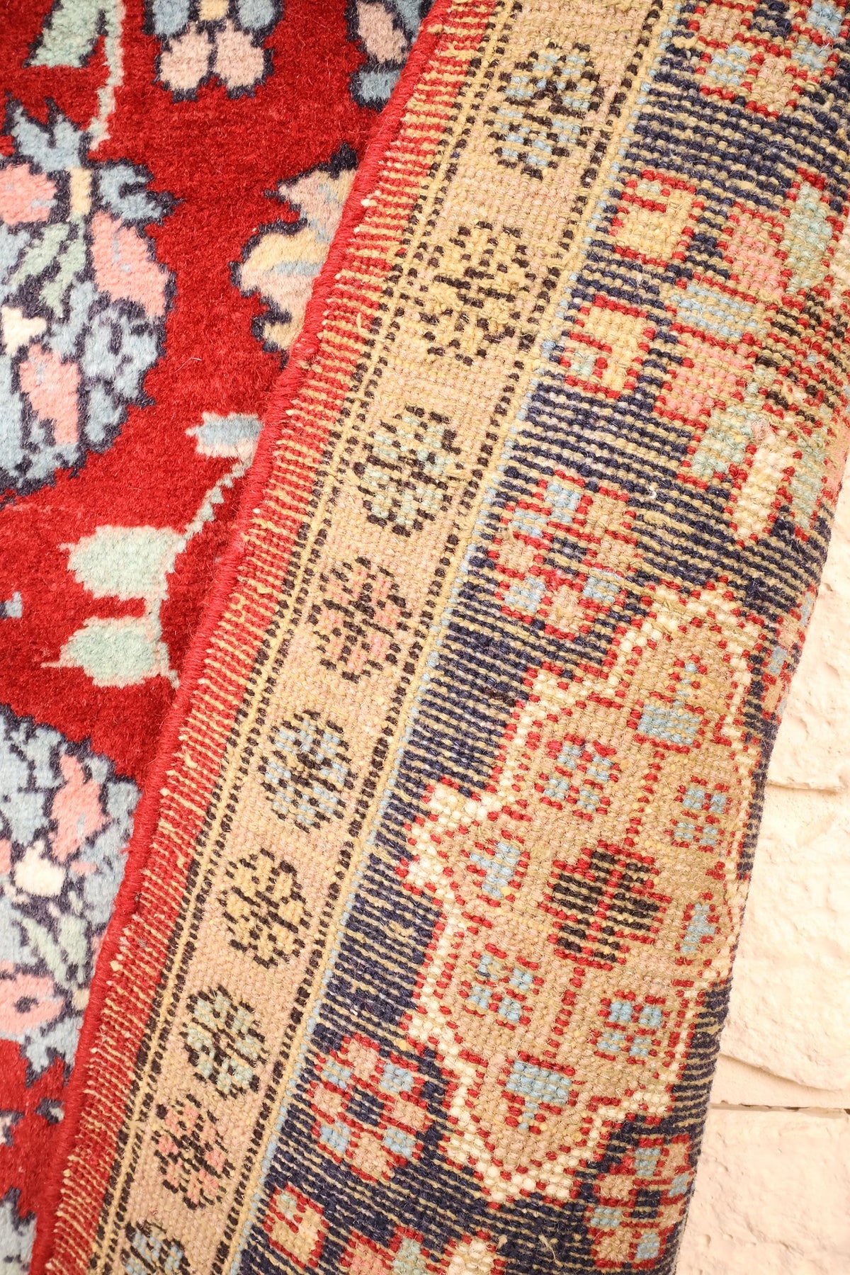Coin replié du tapis Pendjab rouge, envers et rosettes de la bordure beige