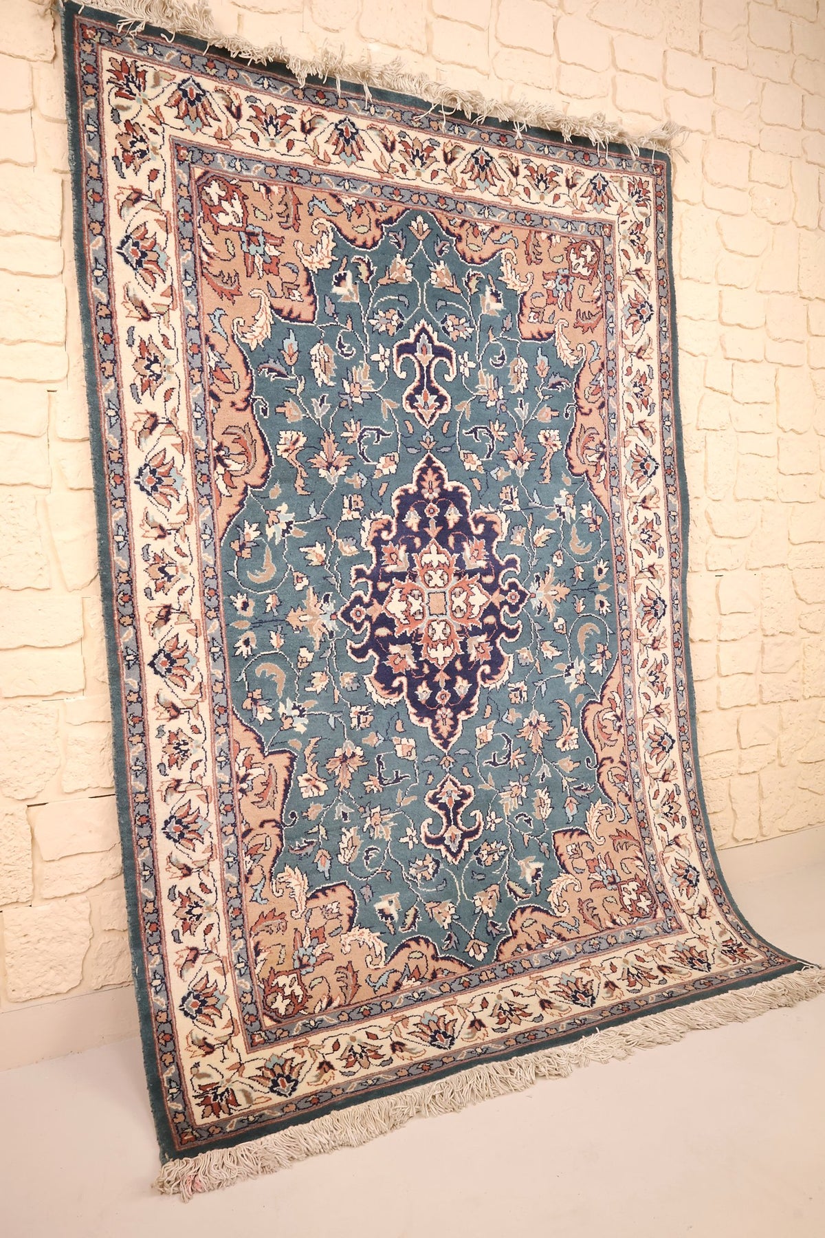 Tapis Pendjab rectangulaire bleu, beige et rose vu de biais contre un mur clair