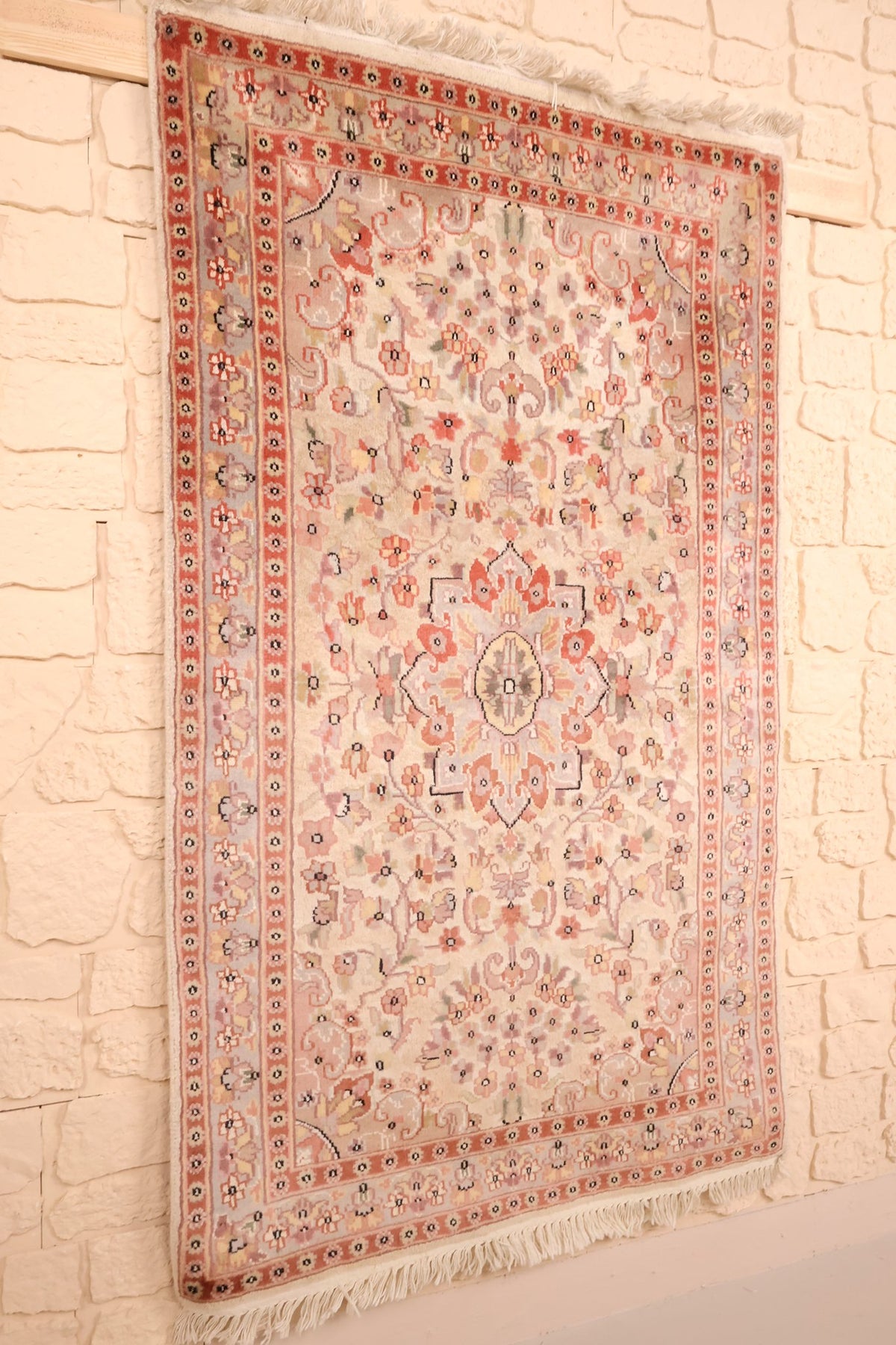 Tapis PLS beige et rose vu de biais, bordures rouge orangé à rosettes
