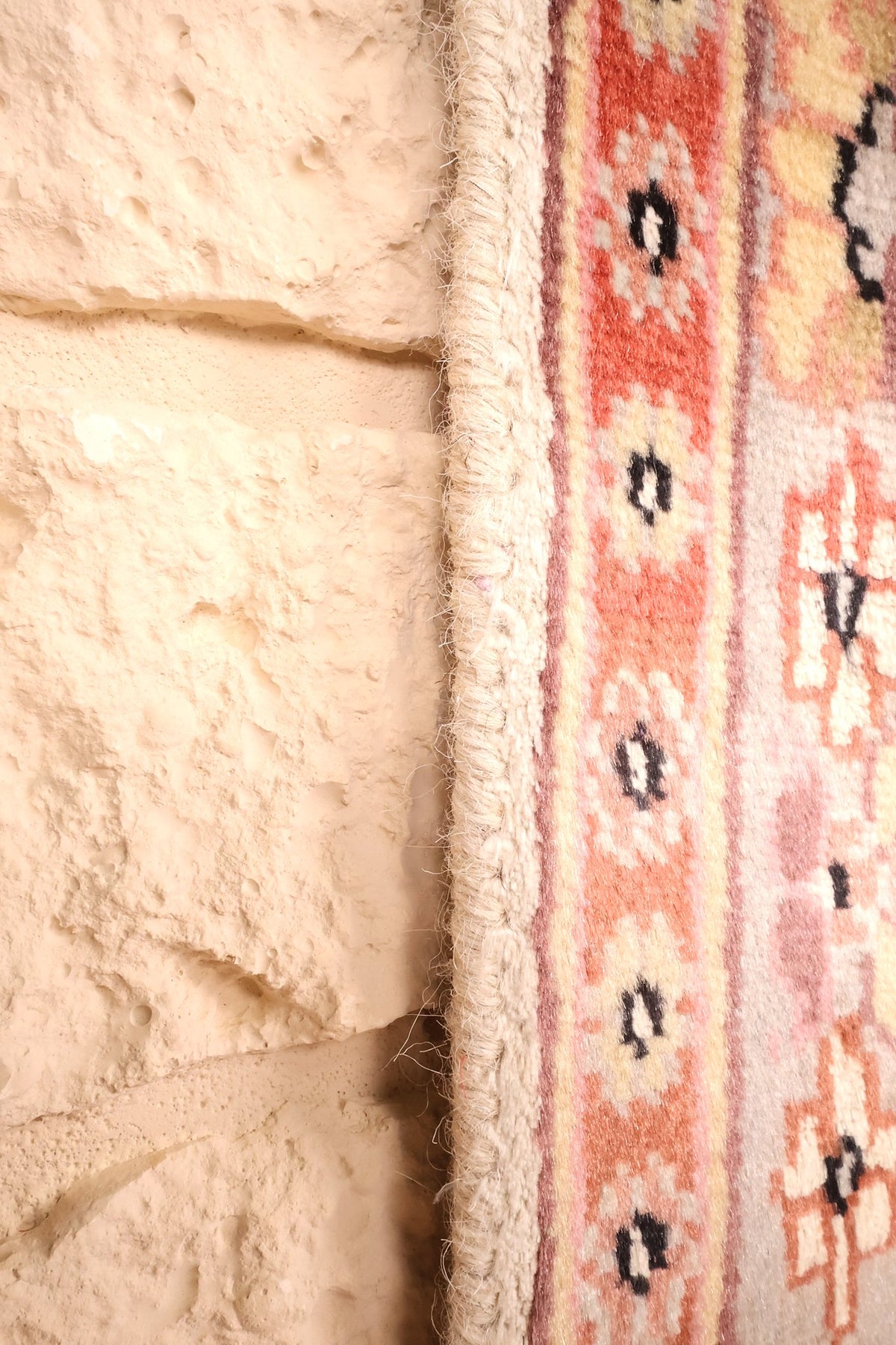 Lisière du tapis PLS beige et rose, bord rectangulaire contre le mur
