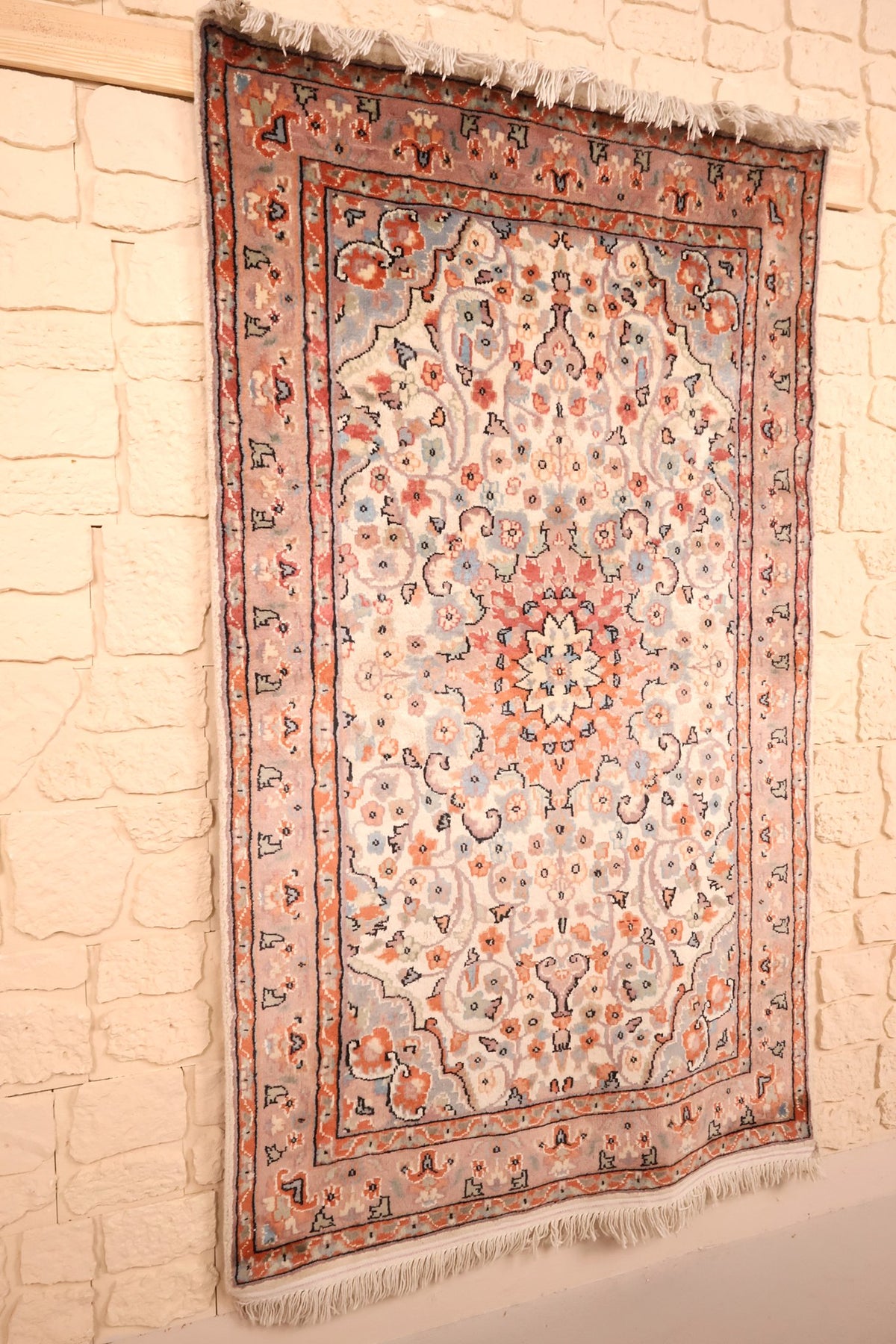 Tapis PLS beige et rose vu de biais, bordures orange et franges blanches