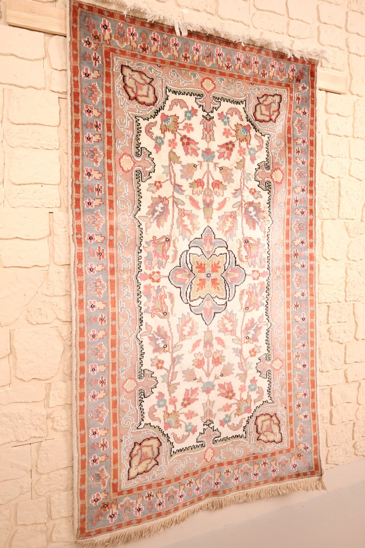 Tapis PLS rectangulaire en laine et soie artificielle, vue de biais contre un mur clair