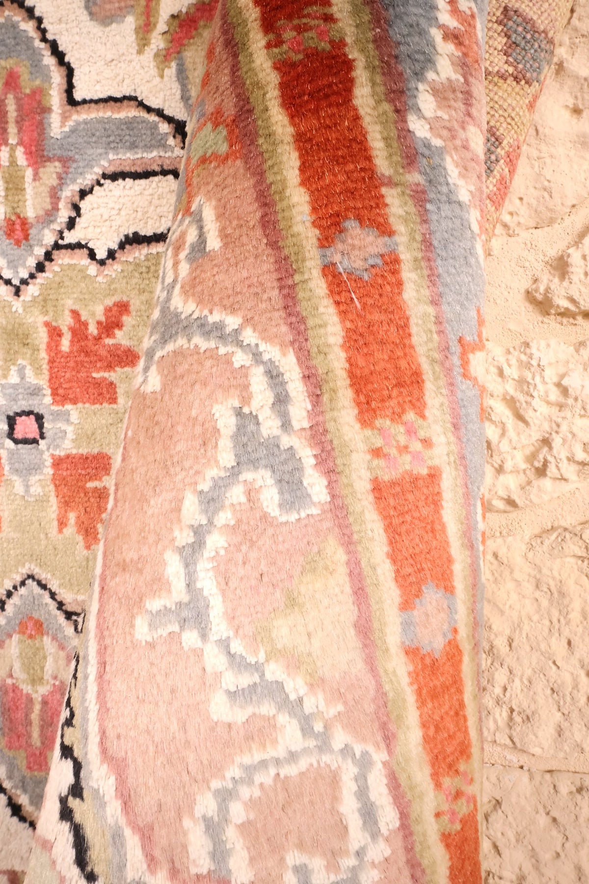 Coin replié du tapis PLS beige, épaisseur et rinceaux blancs de la bande rose