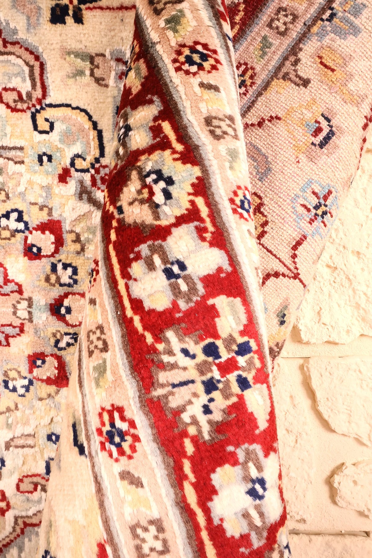 Coin replié du tapis PLS, épaisseur et bordure rouge fleurie visibles