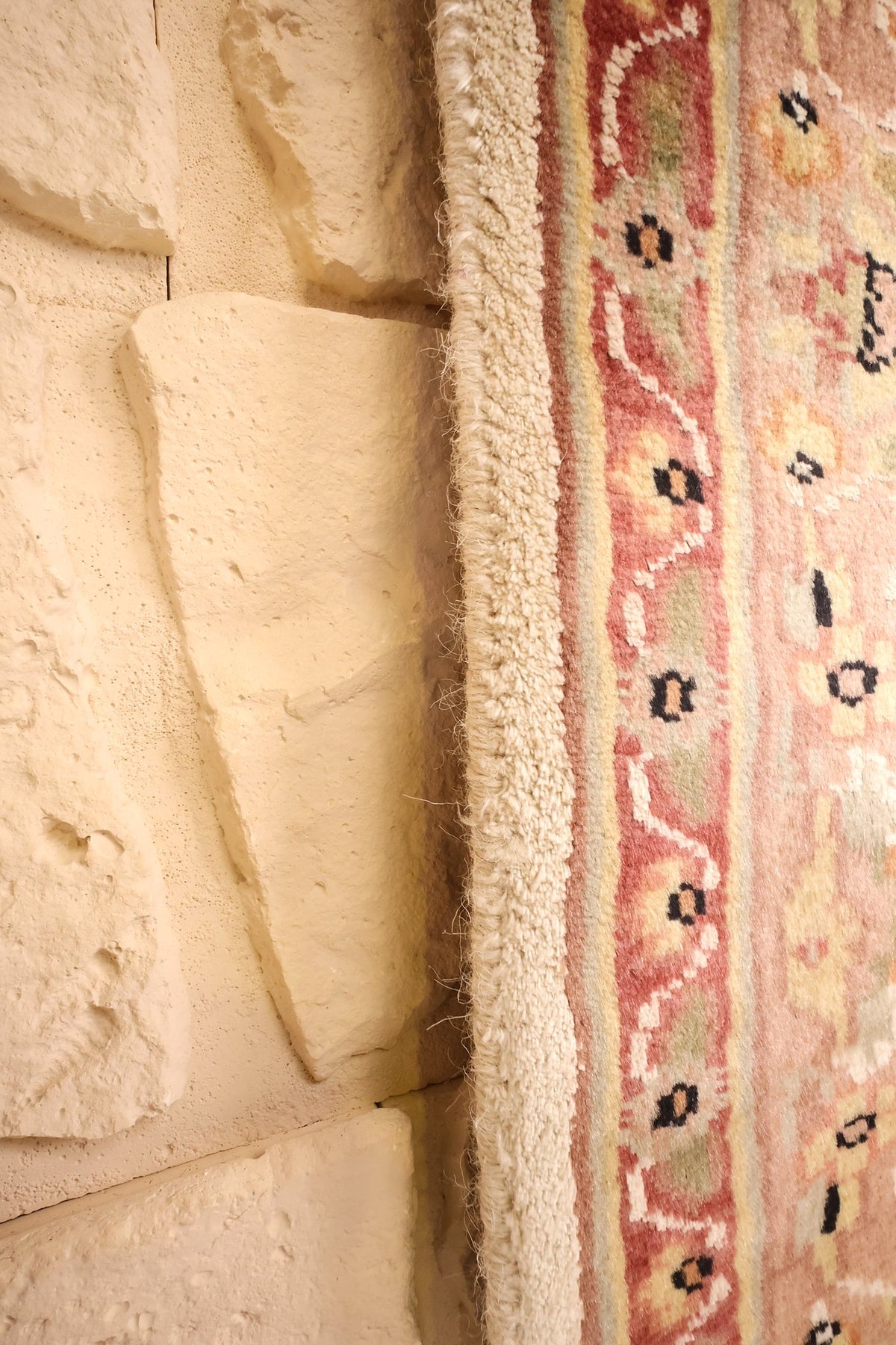 Lisière du tapis PLS beige contre un mur de pierre claire