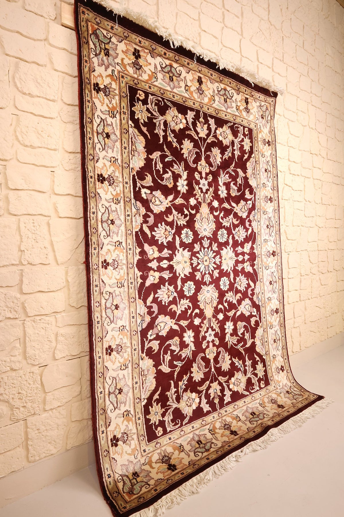 Tapis P. rectangulaire rouge et ivoire vu de biais, dressé contre un mur clair
