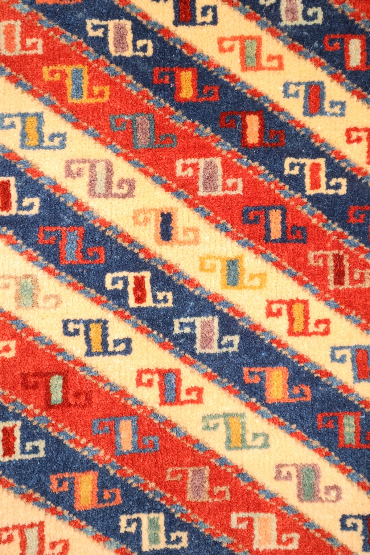 Détail des bandes diagonales rouges, bleu foncé et ivoire à petits crochets du tapis Safir
