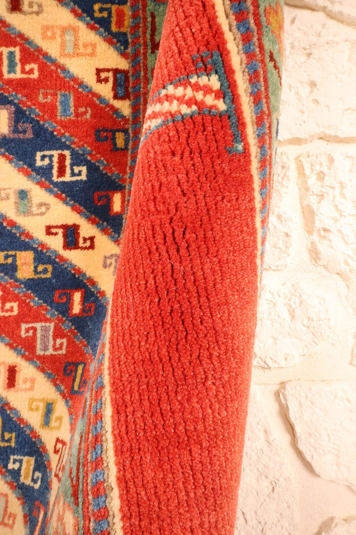 Coin replié du tapis Safir en laine, épaisseur et lisière rouge visibles