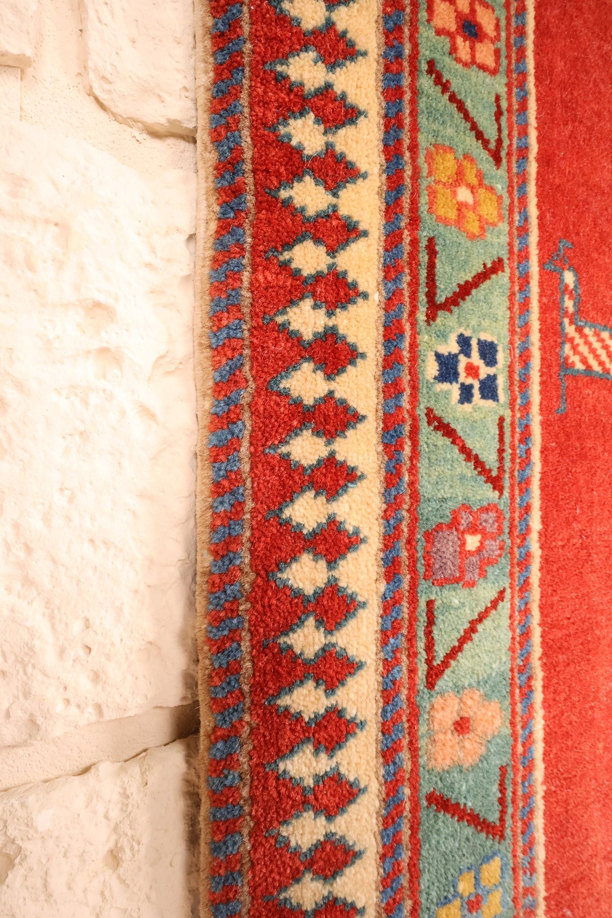 Bordure ivoire à motifs dentelés rouges du tapis Safir, le long du mur clair