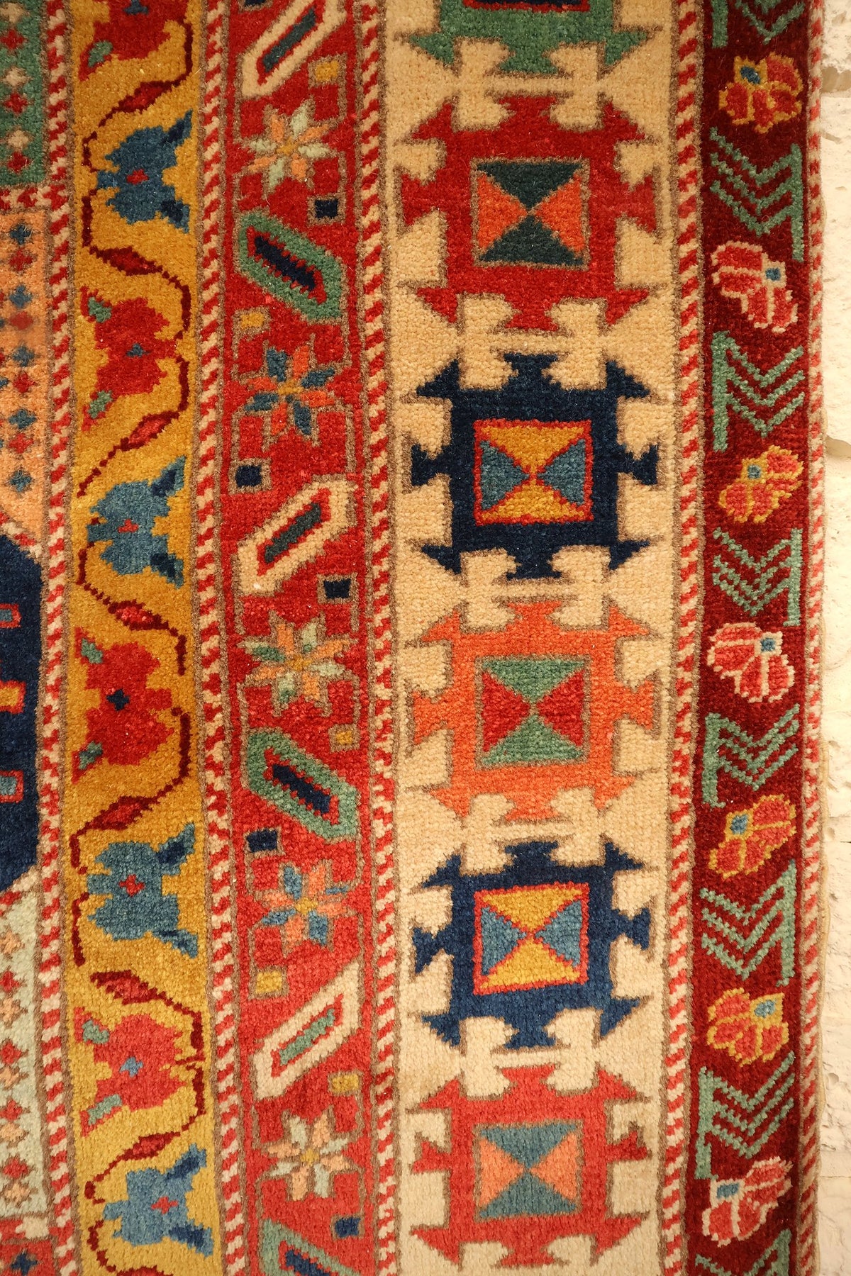 Bordures du tapis Safir : étoiles-croix ivoire, bande jaune à rinceaux, fleurs rouge sombre
