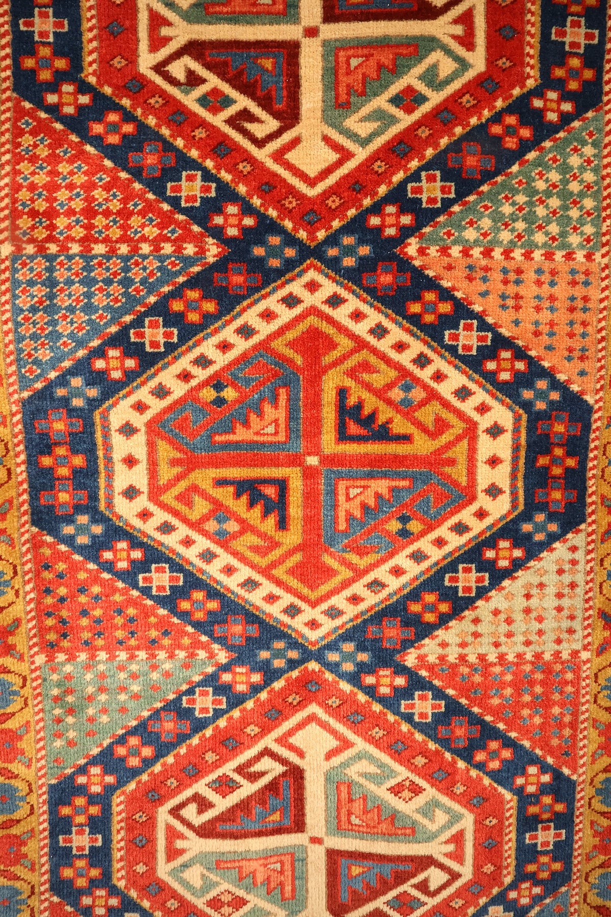 Détail du médaillon central à crochets et motifs en S du tapis Safir rouge et bleu