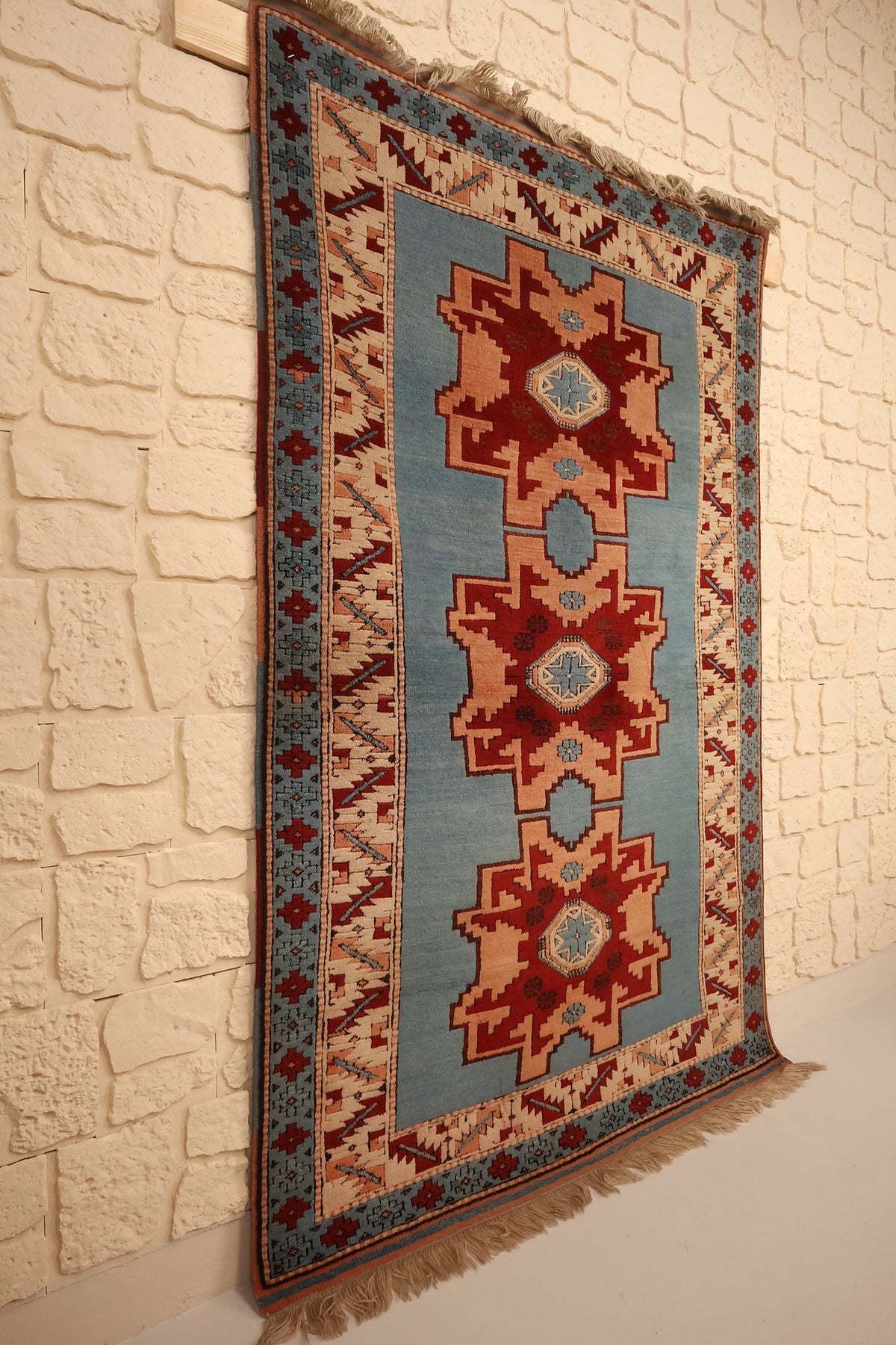 Tapis Shirvan en laine noué à la main, vue de biais contre un mur clair