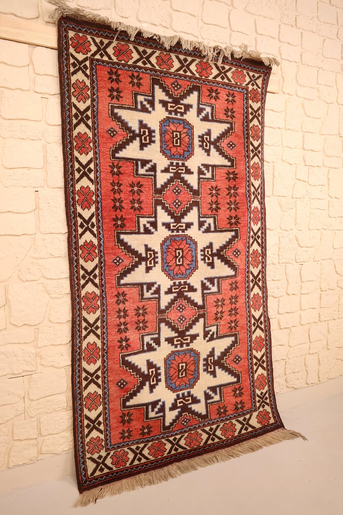 Tapis Shirvan rectangulaire rouge et beige vu de biais, franges écrues aux extrémités