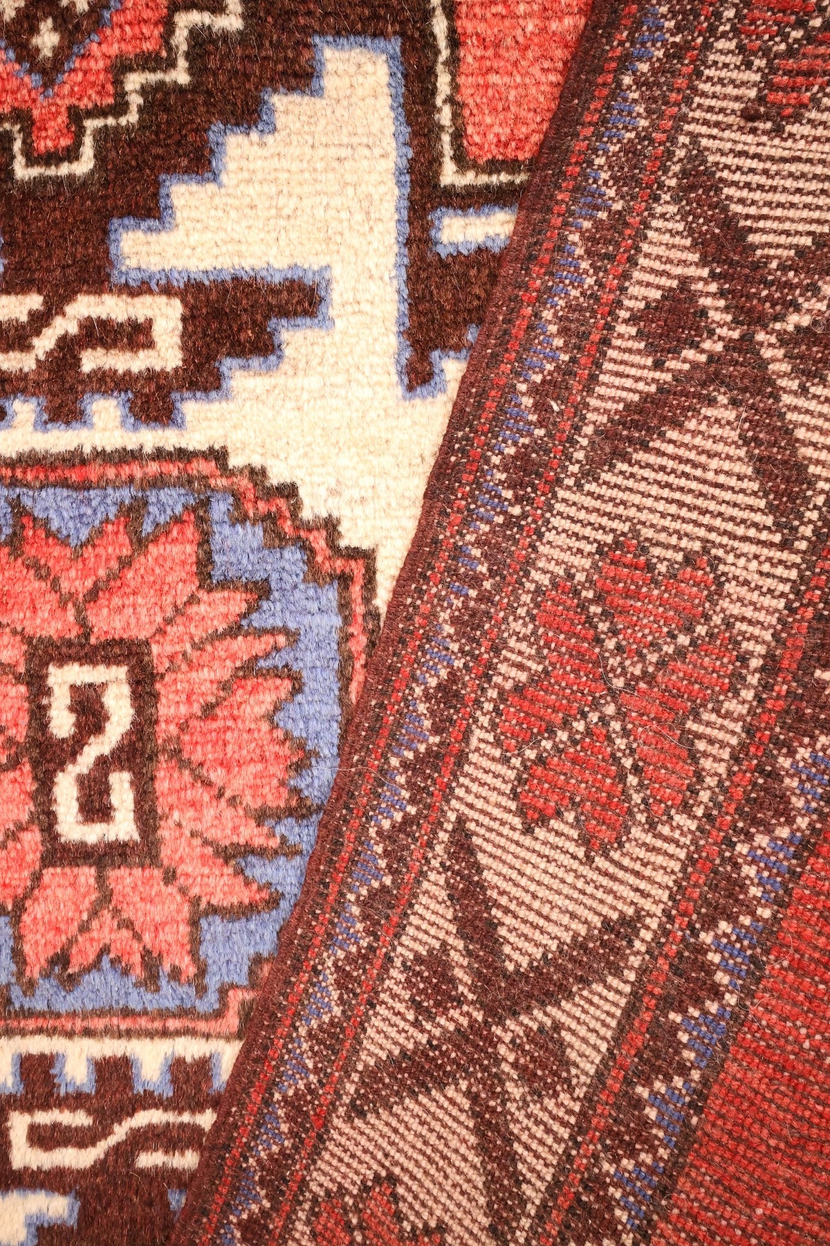 Coin replié du tapis Shirvan rouge, envers et nœuds visibles le long de la bordure