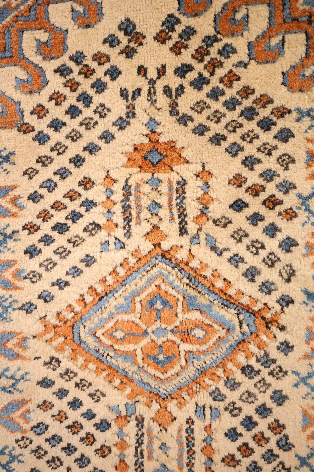Détail du médaillon losangé bleu et orange sur champ beige semé de motifs crochetés