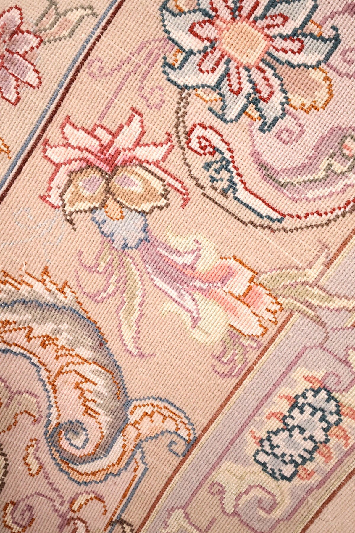 Gros plan des rinceaux fleuris et palmettes sur fond beige rosé, laine et soie naturelle