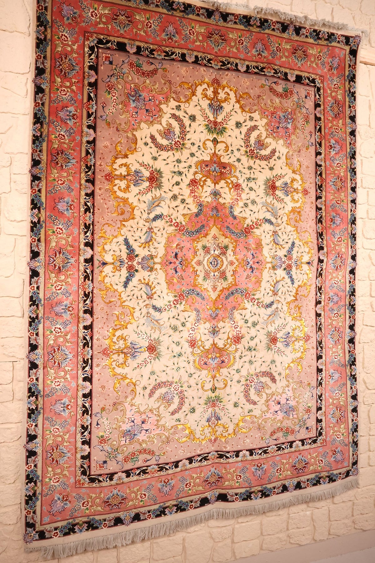 Vue de biais du tapis Tabriz rectangulaire, champ ivoire à rinceaux dorés et bordures roses