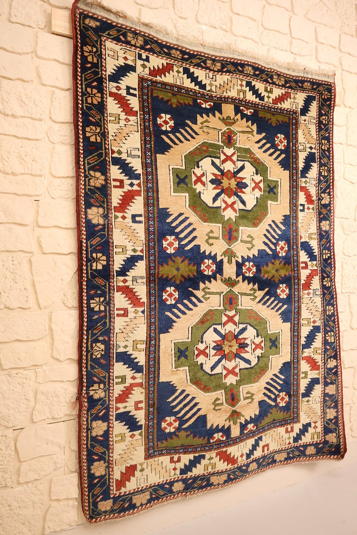 Tapis Tachpinar rectangulaire bleu et beige, vue de biais sur mur clair