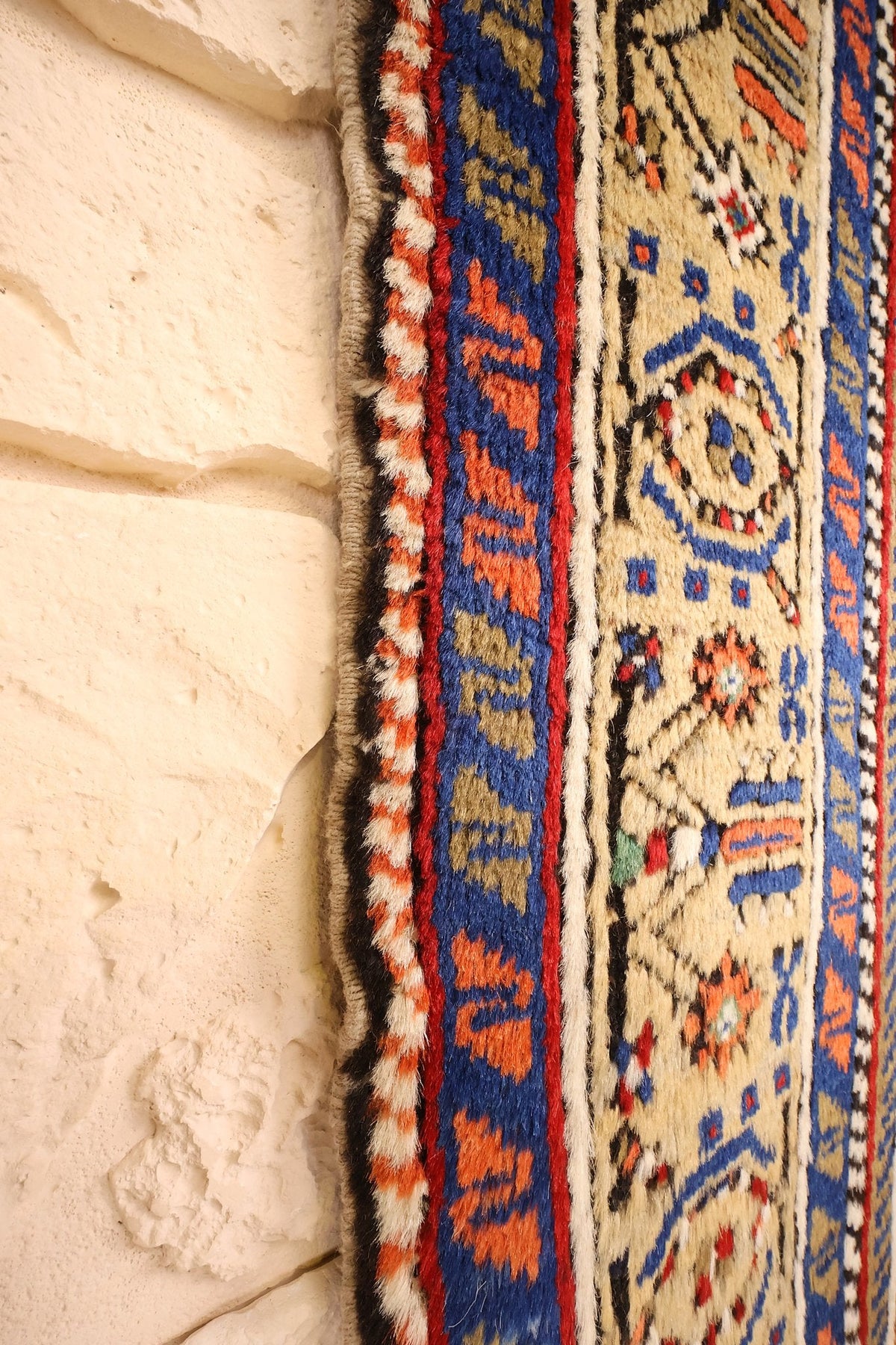 Lisière du tapis Tachpinar orange et bleu, bord vu de près contre le mur