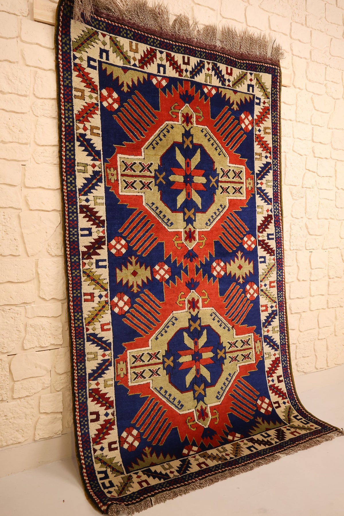 Vue de biais du tapis Tachpinar rectangulaire rouge, bleu et beige, bordure ivoire à chevrons