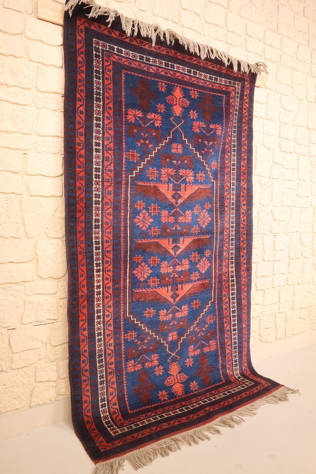 Tapis Yagci Bedir rectangulaire bleu et rouge, vue de biais contre un mur clair