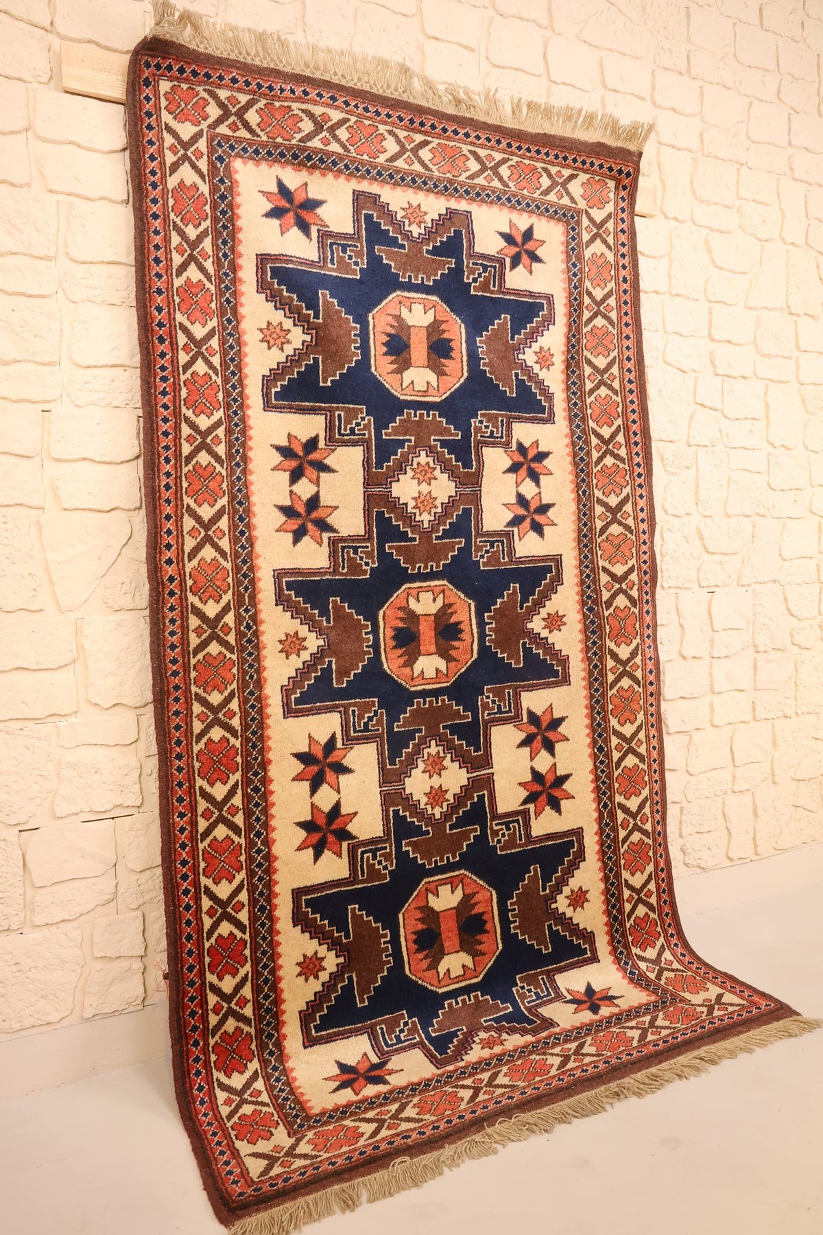 Tapis Yagci Bedir bleu, beige et marron vu de biais, bordure ivoire à rosettes orange
