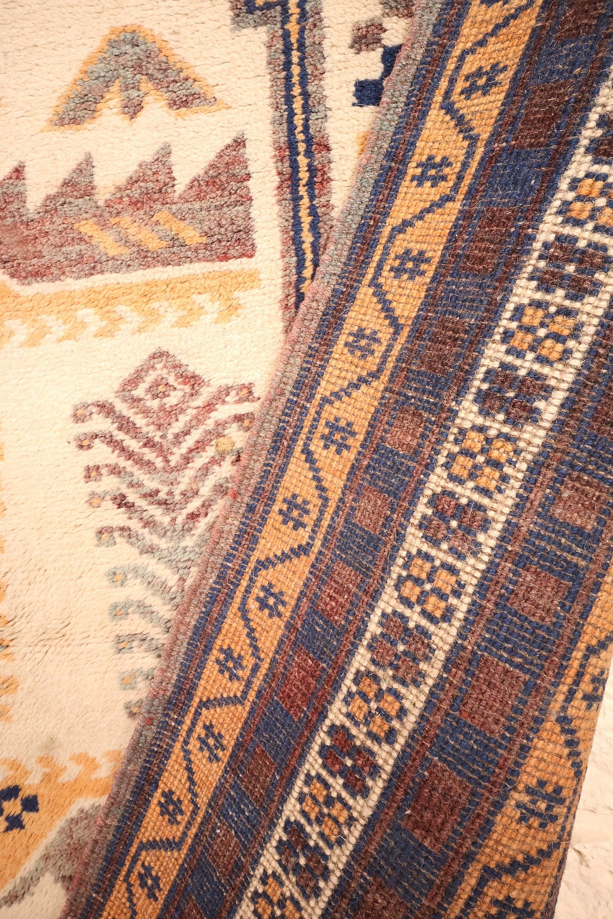 Coin replié du tapis Yagci Bedir, passage du champ beige aux bordures bleu et orange