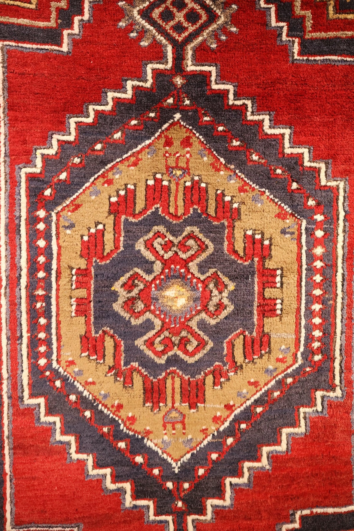 Détail du médaillon central crocheté blanc et rouge sur fond beige du tapis Yahyali