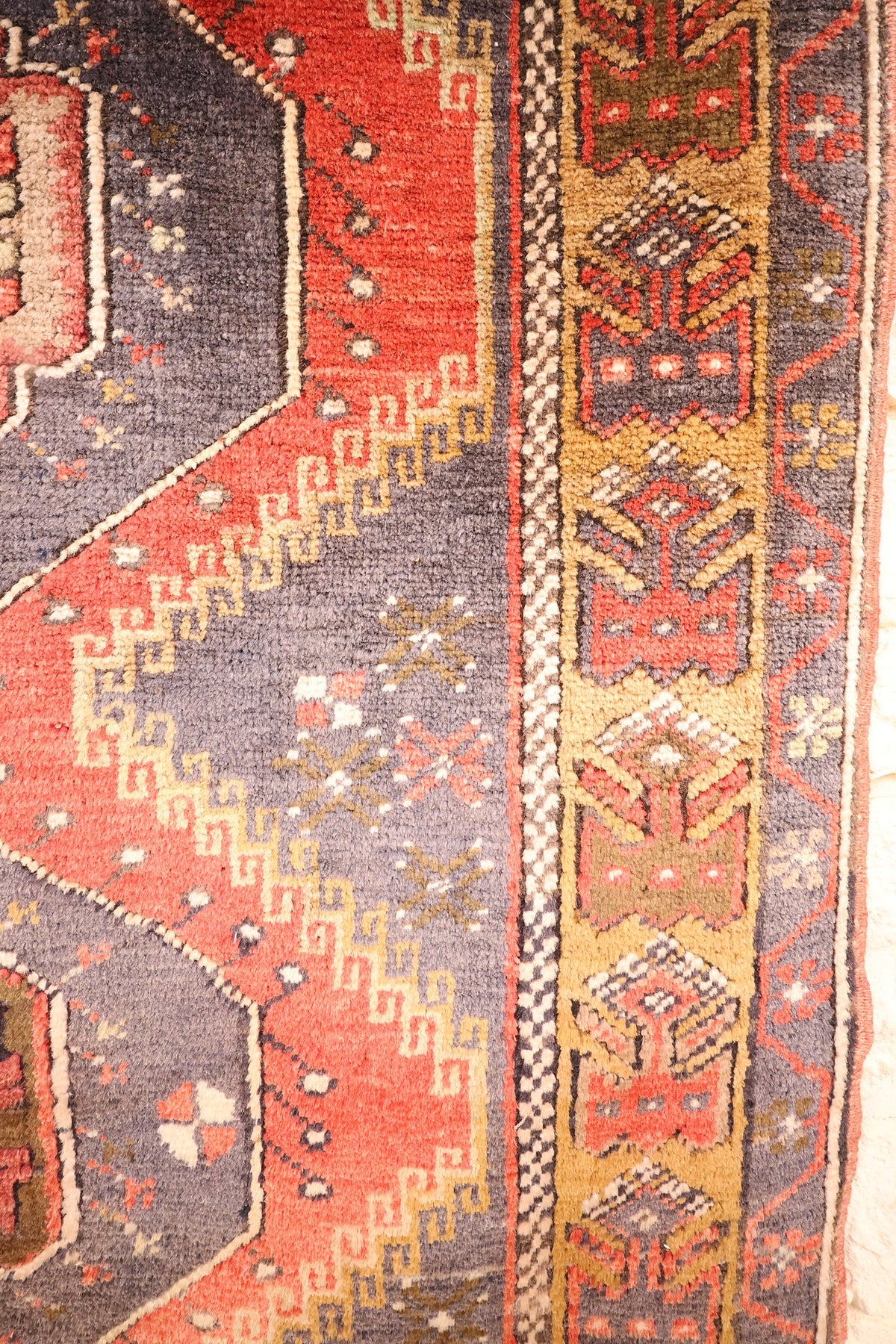Bordure jaune-ocre géométrique et galon en damier du tapis Yahyali rouge