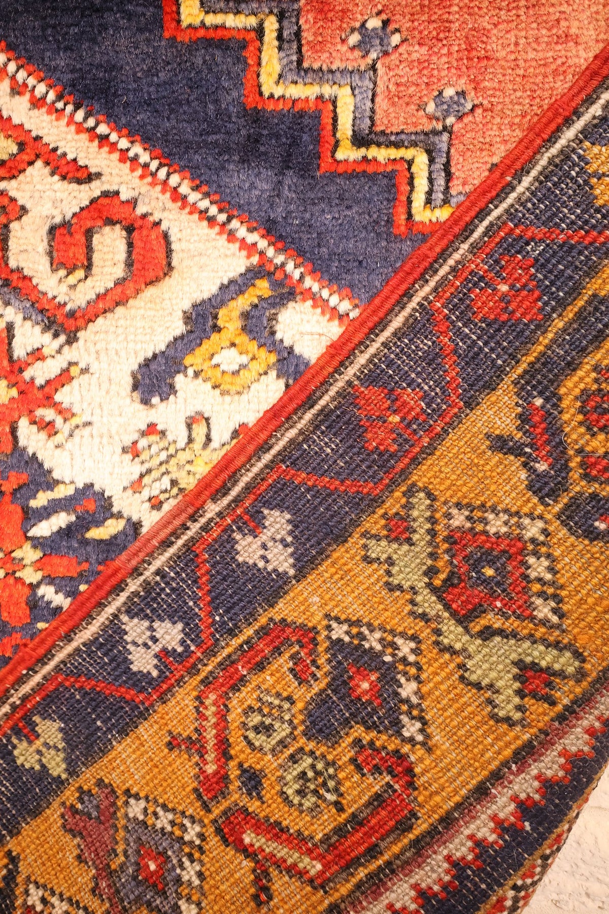 Coin replié du tapis Yahyali, champ bleu nuit et bordure orangée côte à côte