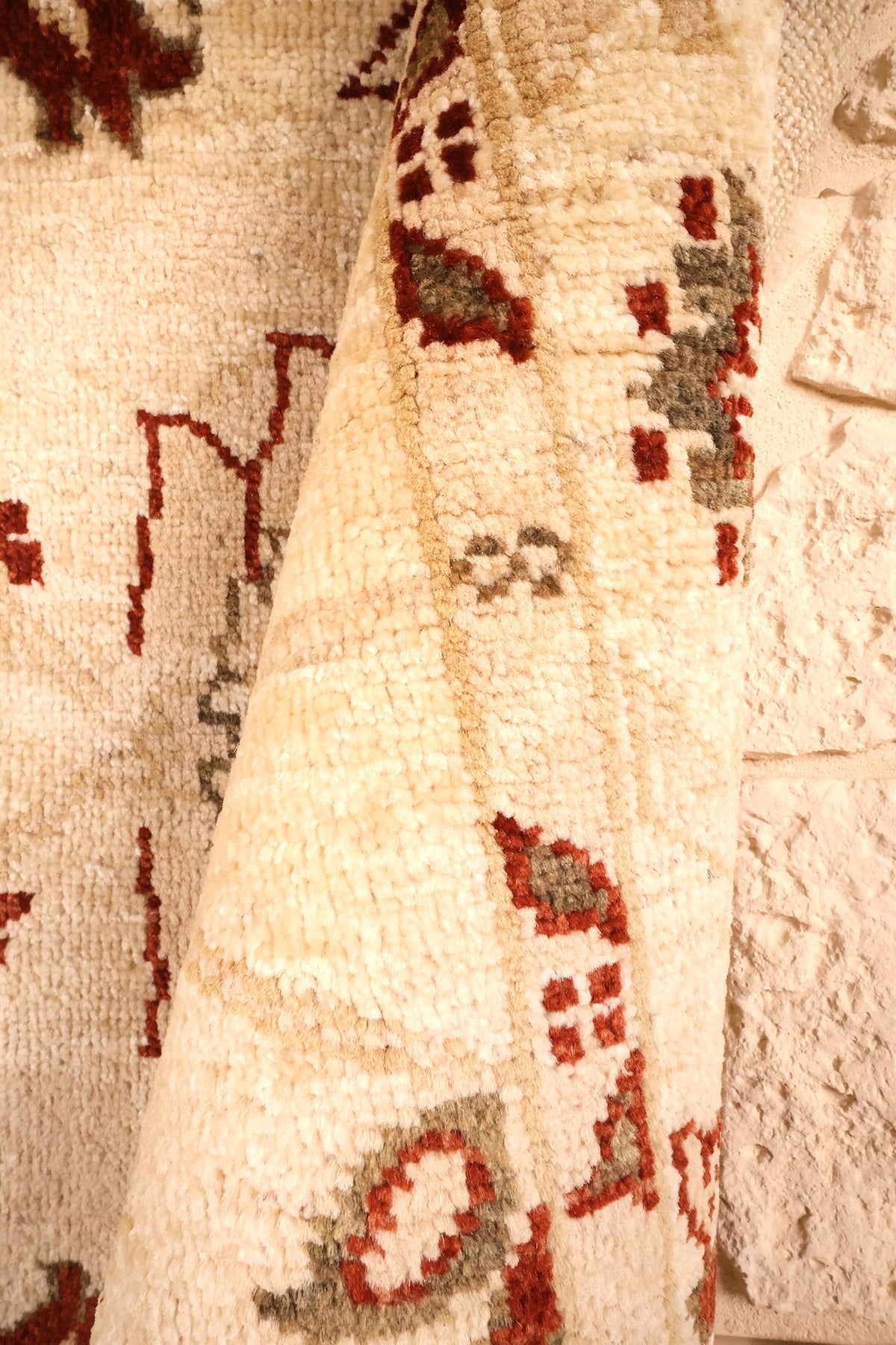 Pli du tapis Ziegler beige montrant l'épaisseur de la laine et les motifs rouges